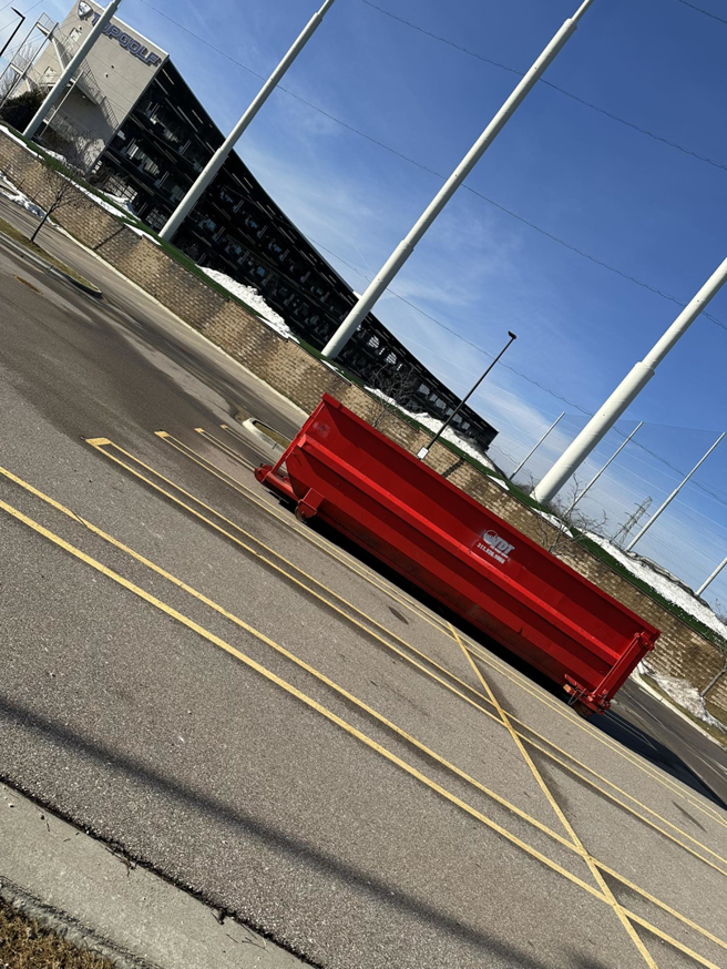 A large red roll-off dumpster from The Dump Town placed in a parking lot in Detroit, MI.
