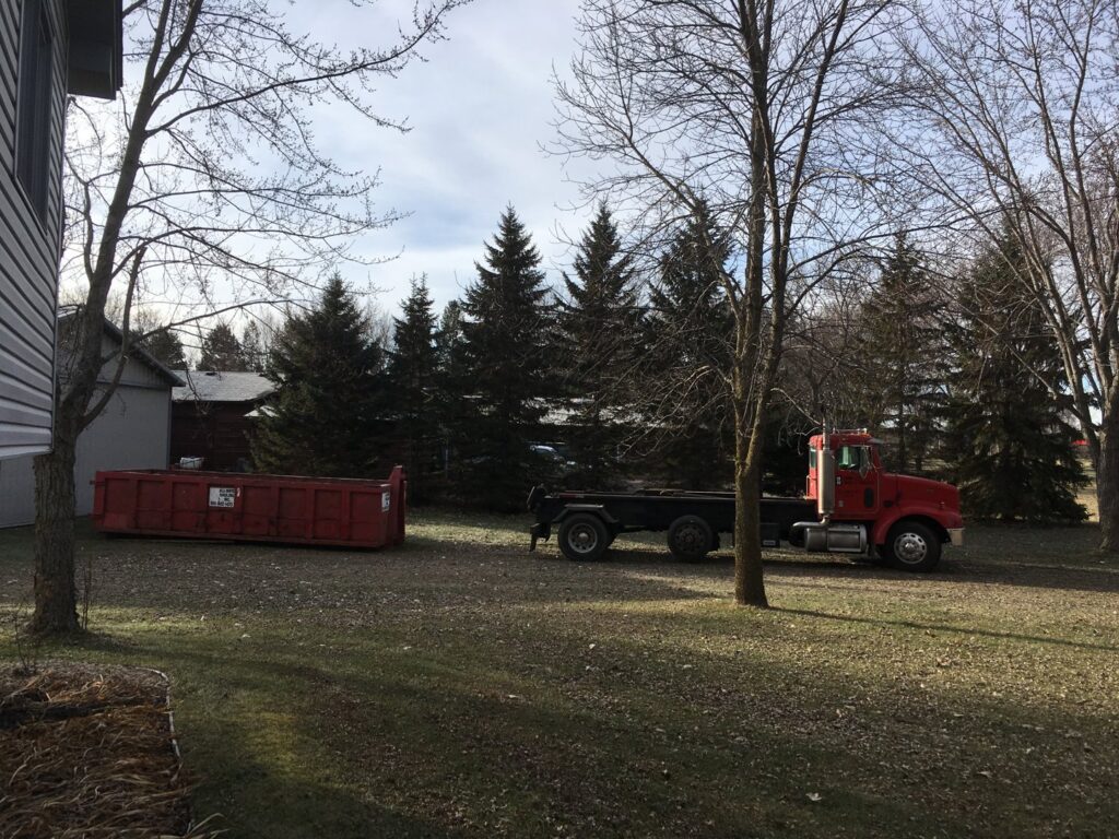 A red roll-off truck and a red dumpster from Minnesota Waste and Transfer placed in a grassy area in Champlin, MN