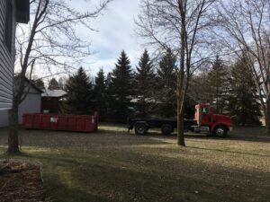 A red roll-off truck and a red dumpster from Minnesota Waste and Transfer placed in a grassy area in Champlin, MN