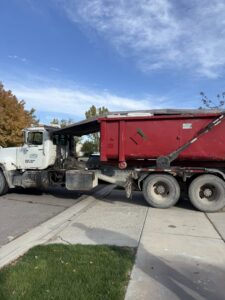 A large red roll-off truck delivering a dumpster for Utah Valley Dumpsters in Provo, UT.