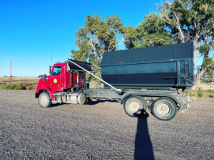 A red roll-off truck with a large dumpster on its back, used for junk removal by First Light Services Llc in Casper, WY.
