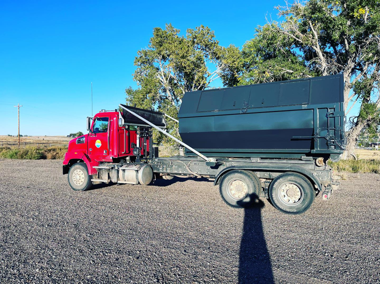 A red roll-off truck with a large dumpster on its back, used for junk removal by First Light Services Llc in Casper, WY.