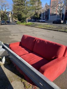 A red sofa left on the side of a street, indicating a need for junk removal services by TrashScouts in Oakland, CA.