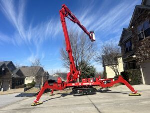 A red spider lift, specialized tree service equipment, parked and stabilized on a residential driveway for Signature Tree Service in Greenville, SC.