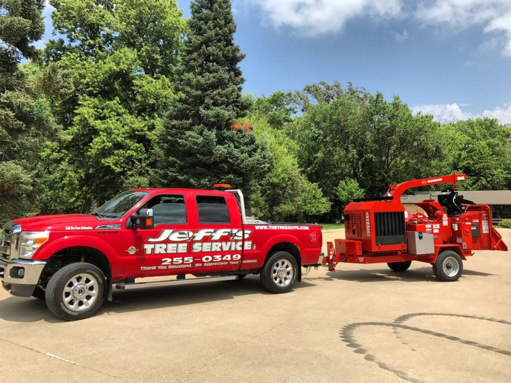 A red Jeff's Tree Service truck towing a large wood chipper, ready for a job in Sioux City, IA.