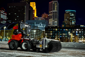 A red utility vehicle with a sweeping brush attachment for property maintenance from Handyman Vehicle Outfitters in Portland, ME.