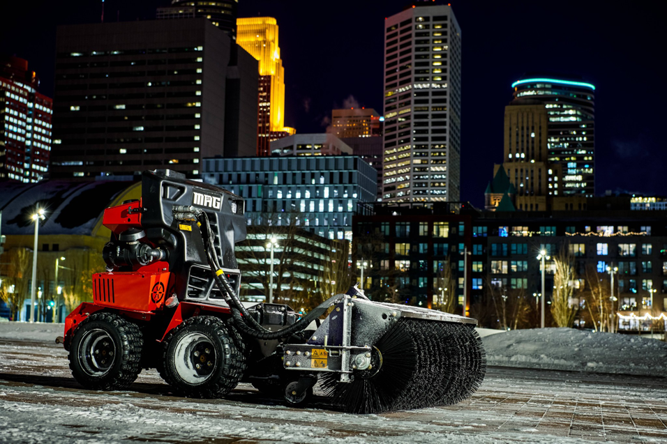 A red utility vehicle with a sweeping brush attachment for property maintenance from Handyman Vehicle Outfitters in Portland, ME.