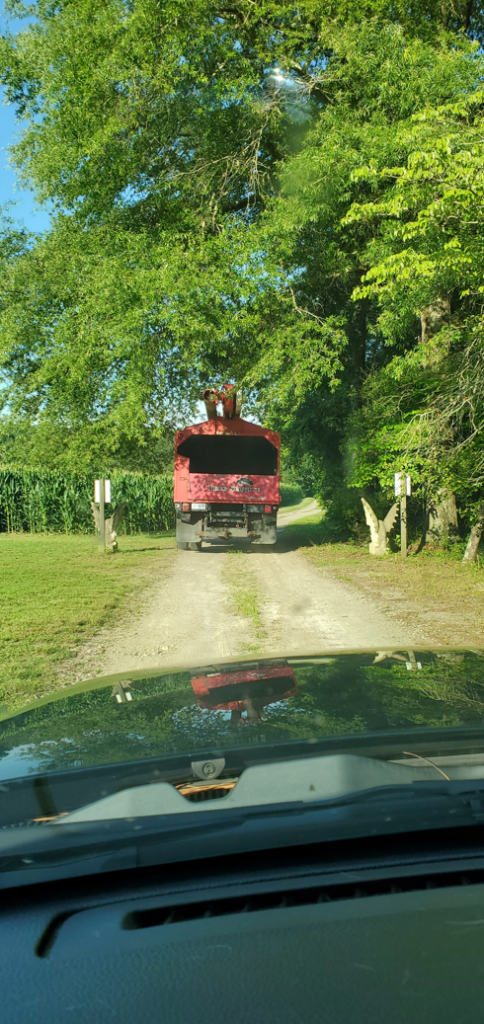 A red wood chipper truck on a dirt road, ready for tree debris removal by Arbor Tree Service, LLC in Zebulon, NC.