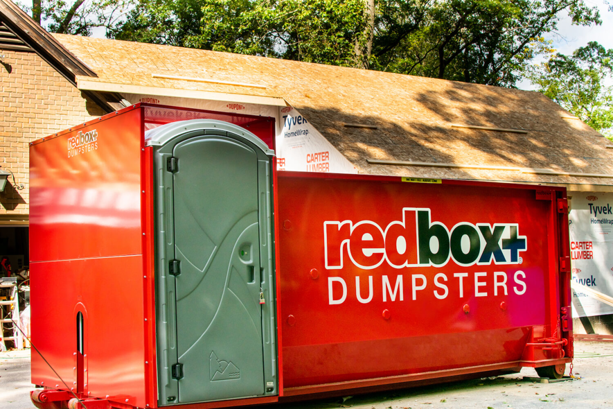 A redbox+ dumpster with a portable toilet placed at a residential construction site in Baton Rouge, LA, by redbox+ of Baton Rouge.