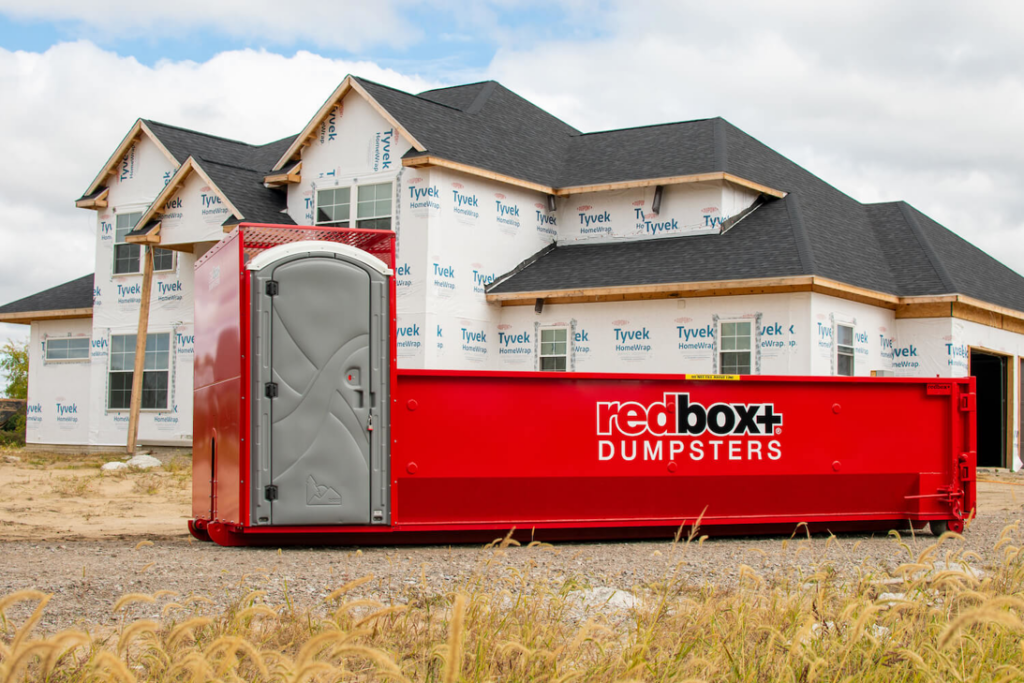 A redbox+ dumpster with a portable toilet at a new home construction site in Baton Rouge, LA, provided by redbox+ of Baton Rouge.