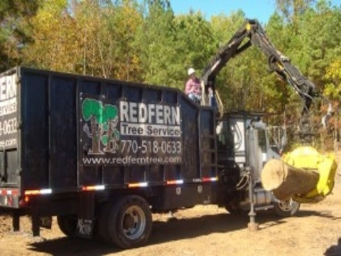 A Redfern Tree Service grapple truck loading large logs into its dump bed in Roswell, GA.