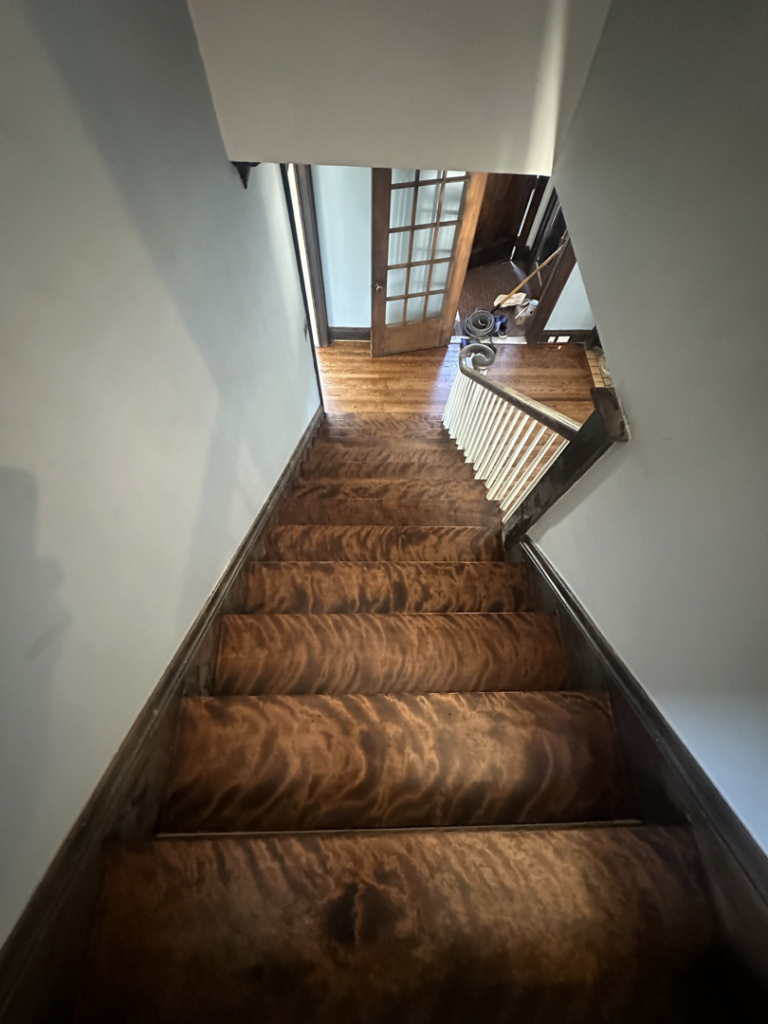 A beautifully refinished wood floor visible at the bottom of a staircase by SANDMAN WOOD FLOOR REFINISHING in Cleveland, OH.