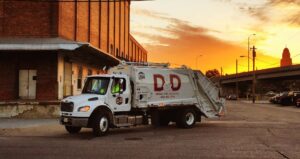 A D&D Refuse Inc. refuse and recycling truck driving on a street at sunset in Lincoln, NE.