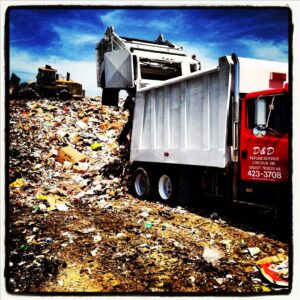 A D&D Refuse Inc. truck at a landfill, surrounded by a large pile of collected refuse in Lincoln, NE.