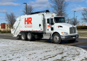 A white Husker Refuse Services truck parked on a snowy day in Lincoln, NE, ready for junk removal.