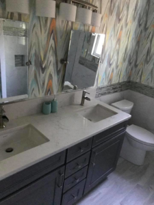 A newly remodeled bathroom featuring a double vanity, modern faucets, and patterned wallpaper by Brown Remodeling And New Construction in Hoover, AL.
