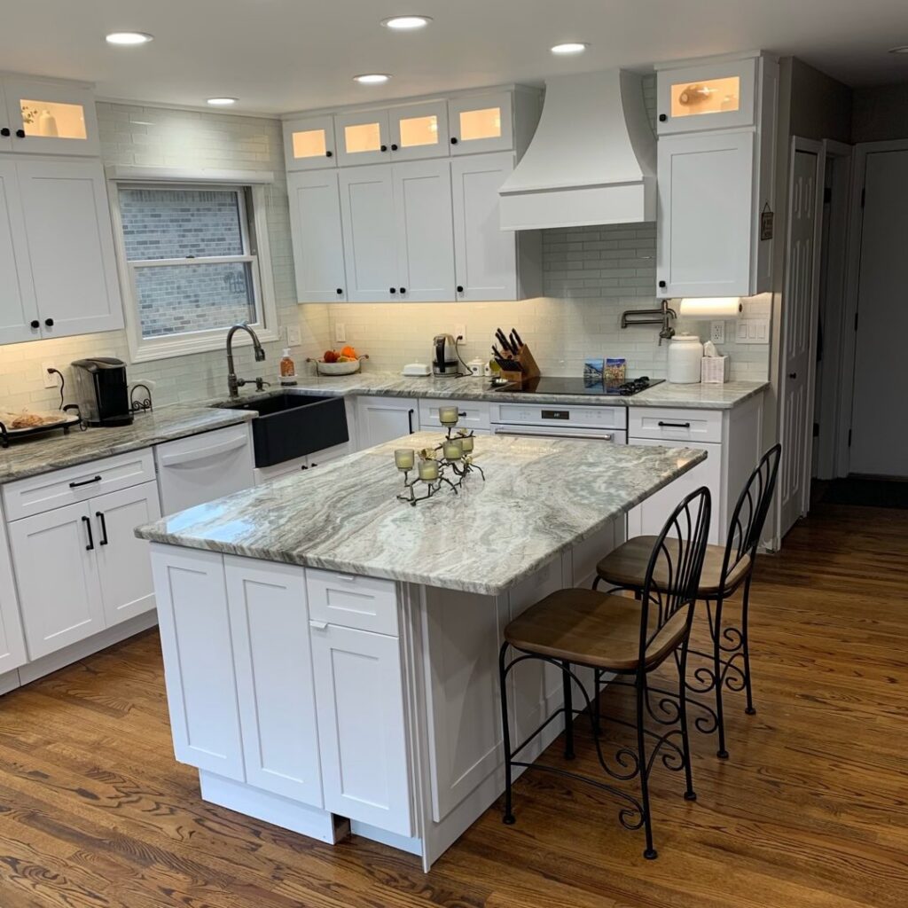 A beautifully remodeled kitchen featuring white cabinets, a large island, and granite countertops by Impressive Basements in Westland, MI.