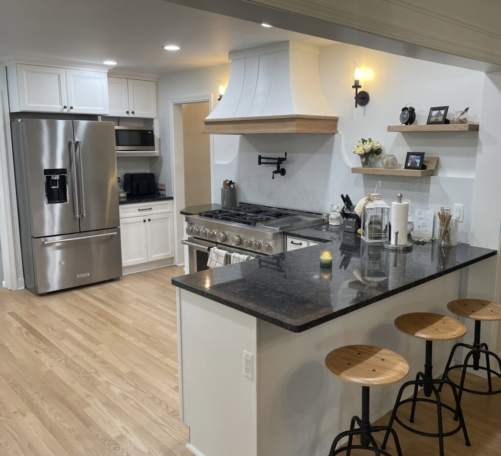 A spacious remodeled kitchen with white cabinets, a professional range, and a dark island by Impressive Basements in Westland, MI.