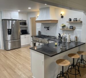 A spacious remodeled kitchen with white cabinets, a professional range, and a dark island by Impressive Basements in Westland, MI.