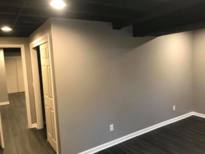 A corner view of a renovated basement room with new flooring and recessed lighting by M Zimmer Construction LLC in Rochester, NY.