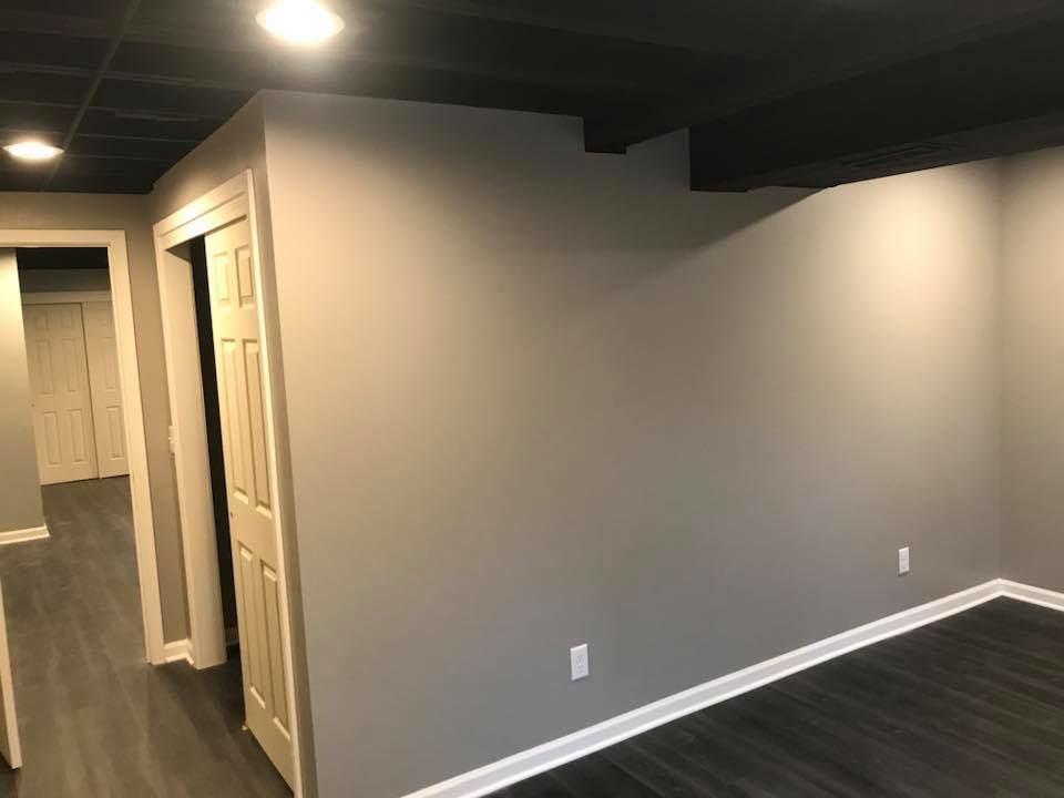 A corner view of a renovated basement room with new flooring and recessed lighting by M Zimmer Construction LLC in Rochester, NY.