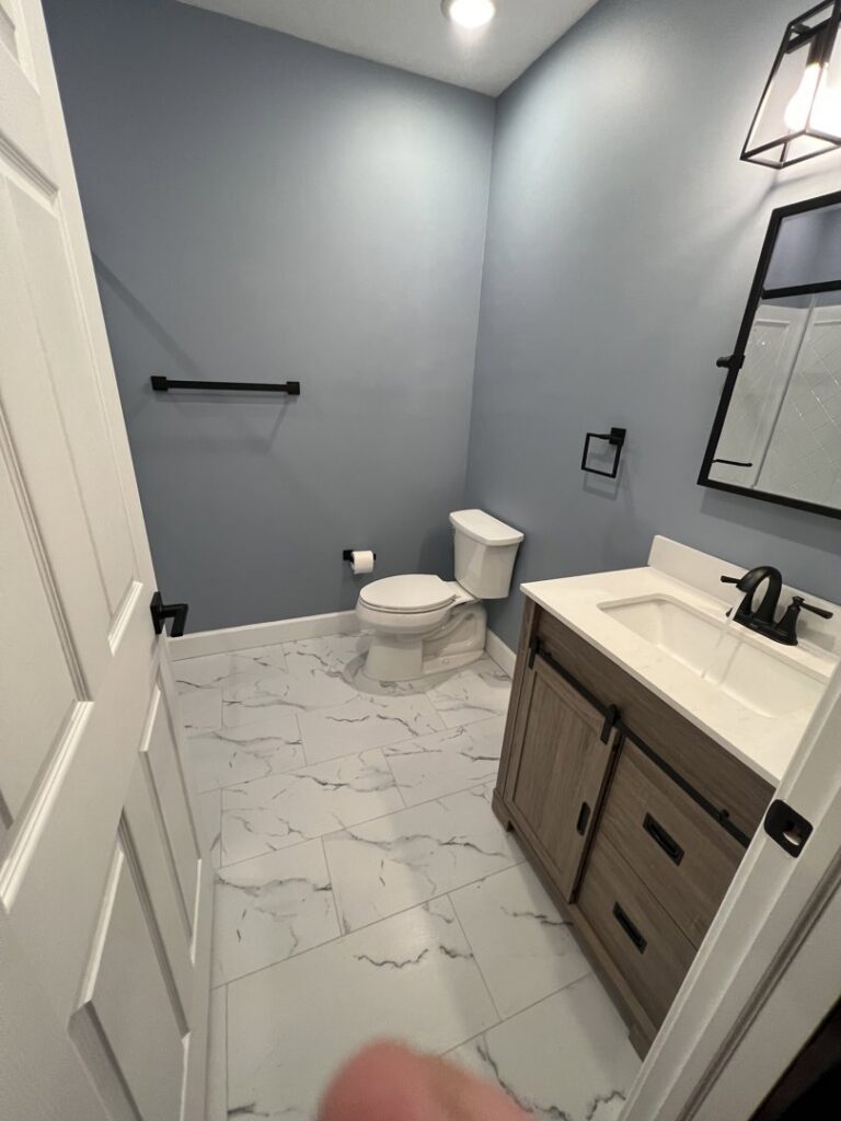 A newly renovated bathroom with blue walls, a modern vanity, and tiled floor, completed by Amaro home improvement llc in Danbury, CT.