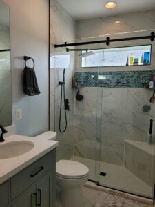 A beautifully renovated bathroom with white marble-look tiles and black fixtures by M J Services Home Remodeling in Gaithersburg, MD.