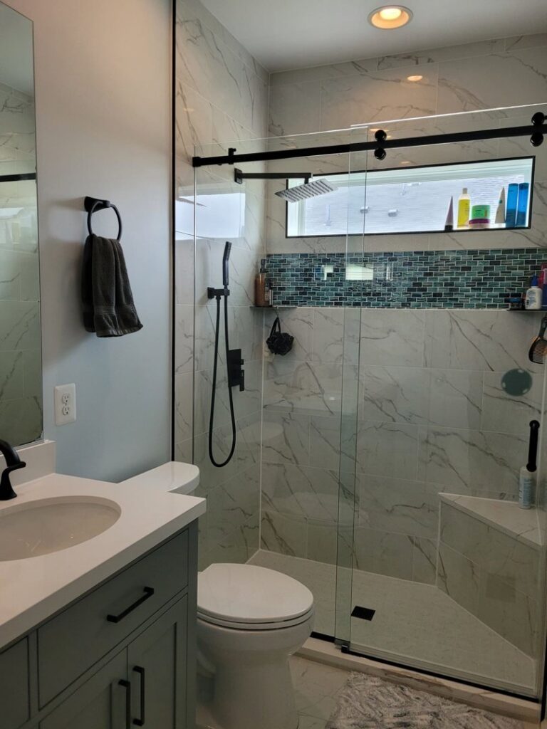 A beautifully renovated bathroom with white marble-look tiles and black fixtures by M J Services Home Remodeling in Gaithersburg, MD.