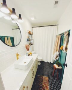 A beautifully renovated bathroom with a modern vanity, round mirror, and black hexagonal floor tiles by Holaway Custom Builds in Fayetteville, AR.