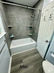 A newly renovated bathroom featuring a white bathtub, grey tiled walls, and modern flooring by RepairTo Roofing, Renovations & Repairs in Wilmington, DE.
