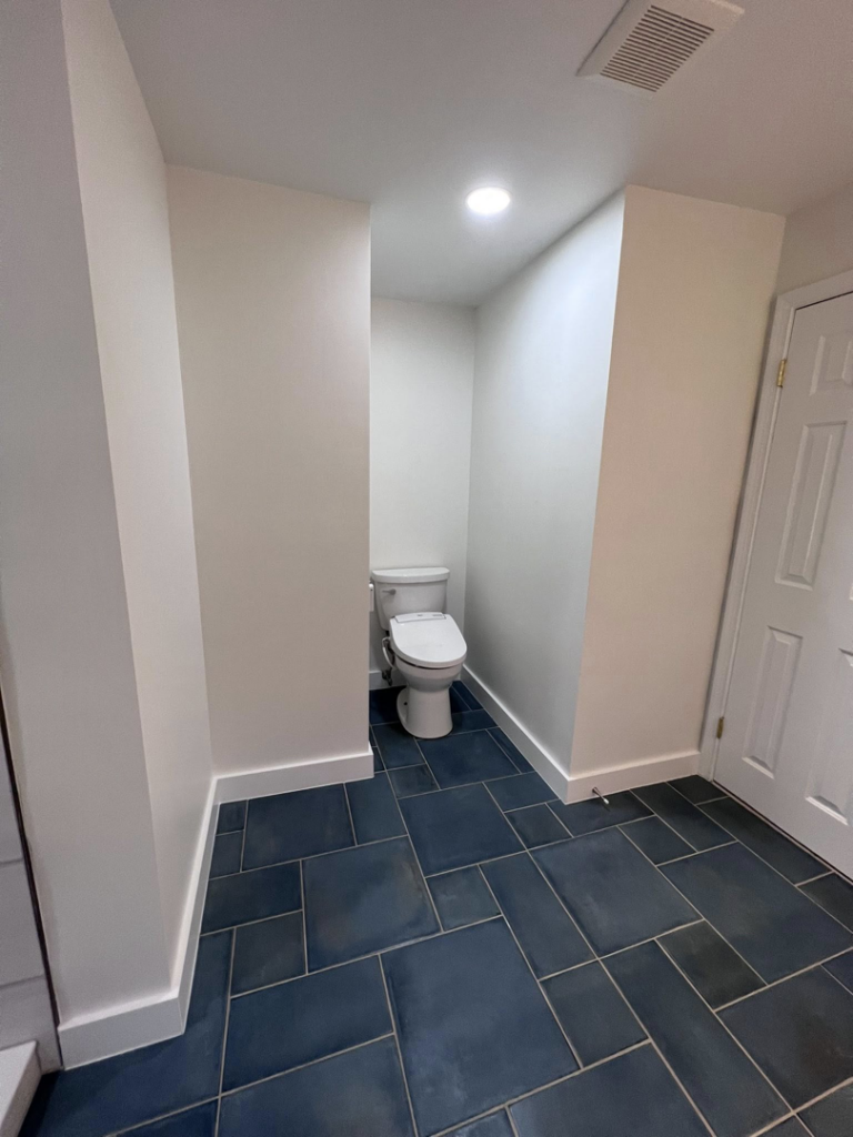 A newly renovated bathroom featuring a modern toilet and dark blue floor tiles, completed by Great Home Construction LLC in Annapolis, MD.