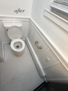 A newly renovated bathroom featuring a white toilet, wainscoting, and new flooring, completed by NOAT in North Providence, RI.