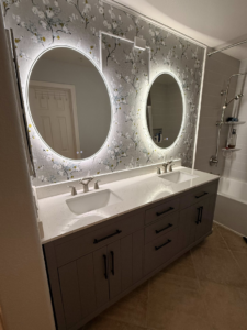 A beautifully renovated bathroom vanity with double sinks and illuminated mirrors by Pauda Handyman in San Diego, CA.