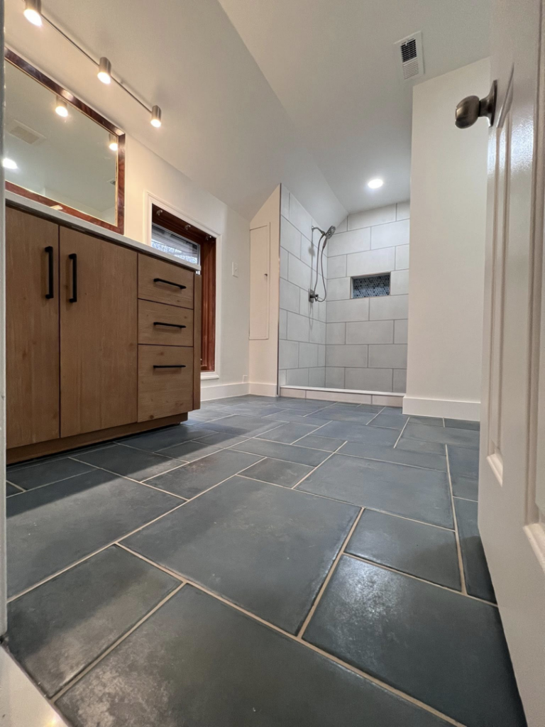 A newly renovated bathroom featuring a modern wooden vanity, mirror, and tiled shower, completed by Great Home Construction LLC in Annapolis, MD.