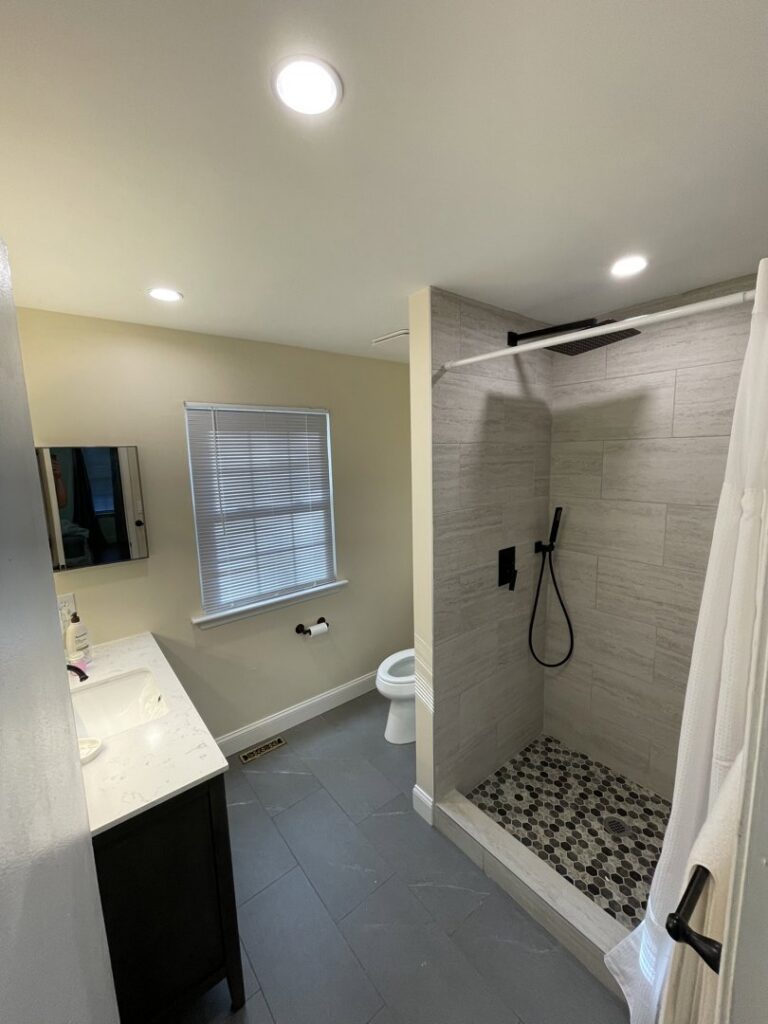 A renovated bathroom featuring a modern walk-in shower, dark vanity, and bright recessed lighting by RepairTo Roofing, Renovations & Repairs in Wilmington, DE.