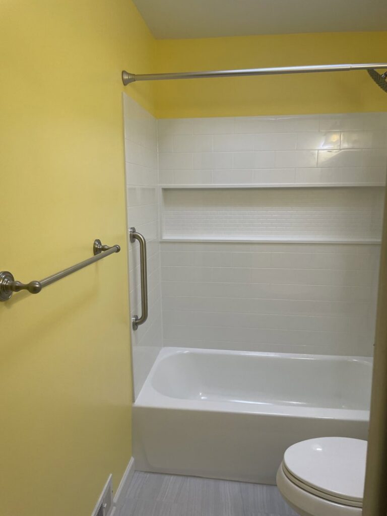 A renovated bathroom featuring a new white bathtub, built-in shelving, and bright yellow walls by MPH Design in Philadelphia, PA.
