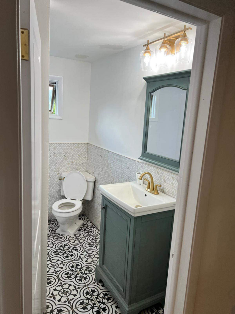 A newly renovated small bathroom featuring a green vanity, gold faucet, and patterned floor tiles by J&A Contractor LLC in Milwaukee, WI.