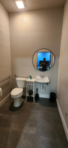 A renovated bathroom featuring a round mirror, new sink, toilet, and dark floor tiles by Fine Point Construction LLC in Medford, OR.