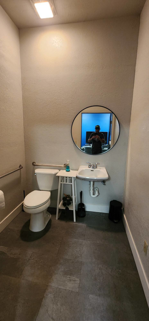 A renovated bathroom featuring a round mirror, new sink, toilet, and dark floor tiles by Fine Point Construction LLC in Medford, OR.