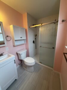 A renovated bathroom featuring a modern sliding glass shower door, new vanity, and light pink walls by MPH Design in Philadelphia, PA.