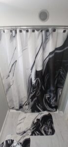 A renovated bathroom featuring a tiled shower with a black and white marble-patterned curtain and matching bath mats by Prime Construction And Flooring in Lorain, OH.