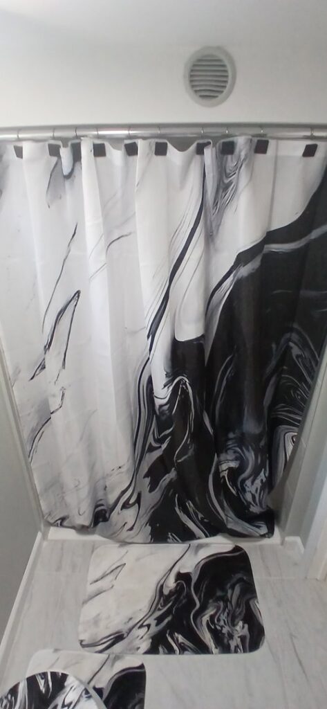 A renovated bathroom featuring a tiled shower with a black and white marble-patterned curtain and matching bath mats by Prime Construction And Flooring in Lorain, OH.