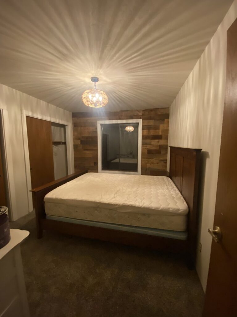 A newly renovated bedroom featuring wooden wall paneling and a modern light fixture by The Handy Nevadan LLC in Reno, NV.