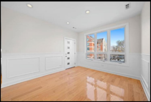 A newly renovated empty room with gleaming hardwood floors and fresh white walls by Revival Home Remodeling in Chicago, IL.