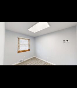 A renovated empty room with new paint on the walls and fresh laminate flooring, showcasing work by EJ Drywall Plus in Kearney, NE.