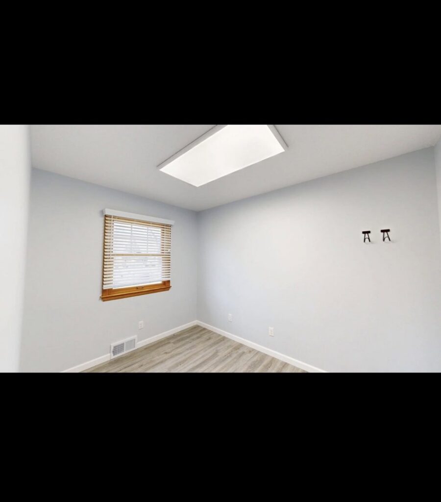 A renovated empty room with new paint on the walls and fresh laminate flooring, showcasing work by EJ Drywall Plus in Kearney, NE.
