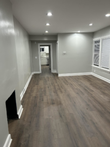 A renovated living room with new wood-look flooring and freshly painted walls, completed by CJ Flooring LLC in Flat Rock, MI.