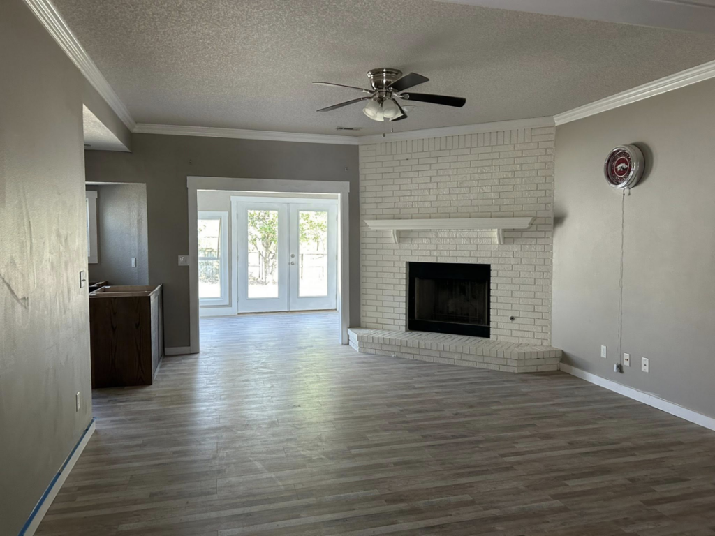 A renovated living room with new flooring, painted walls, and a white brick fireplace by Old Things Created New Handyman Service in Springdale, AR.