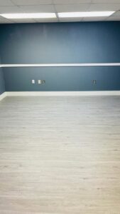 A newly renovated room featuring dark blue walls, white trim, and light wood-look laminate flooring by SD Masters in Miami, FL.