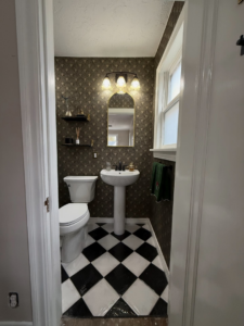 The entrance view of a newly renovated small bathroom with black and white tiled floor by Waking Up Construction in Oklahoma City, OK